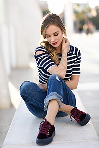 金发女人,时尚模特,坐城市背景的长凳上,闭着眼睛体贴的轻女孩穿着条纹T恤蓝色牛仔裤街上漂亮的俄罗斯女,辫子图片