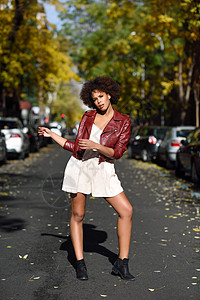 轻的黑人女,留着AFRO发型,站城市街道上混合女人穿红色皮夹克白色连衣裙与城市背景图片