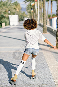 站溜冰鞋上的黑人妇女户外骑着棕榈树的海滩长廊上阳光明媚的日子里,女孩阿弗罗的发型翻滚图片