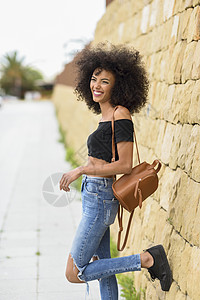 微笑的混血女人站街上快乐的混合女人AFRO的头发站户外女穿着休闲服装城市背景生活方式的图片