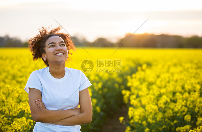 户外肖像金色的黄昏阳光下美丽的快乐混合种族非裔美国女孩十几岁的女轻女子微笑快乐,望向天空的黄色花朵混血非裔美国女孩少图片