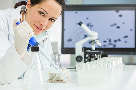 位女医学科学研究员科学家,实验室里用吸管烧瓶,身后台电脑器实验室用吸管烧瓶的女研究科学家图片