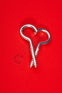 两个螺旋螺栓以心脏的形式铺设红色的背景上钢铁般的心图片