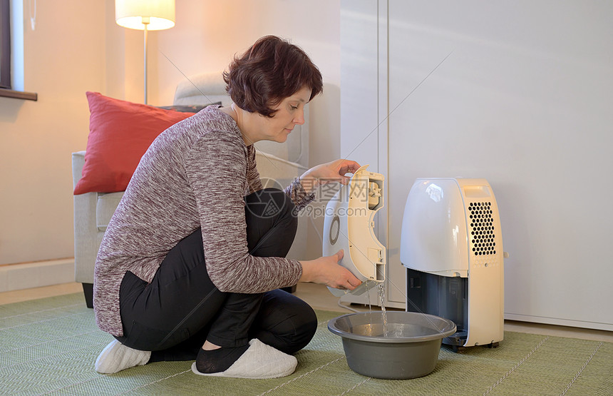 带便携式除湿器的女人收集水图片