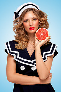 美丽的轻女子穿着水手服,着个红色的葡萄柚,抗衰老的机护肤治疗身体脸的蓝色背景图片