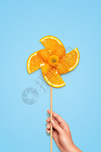蓝色背景下由新鲜橙色切片制成的黄色玩具风车的创造静物生活图片