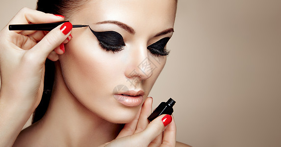 化妆师应用眼影美丽的女人化妆眼与黑色衬里时尚化妆箭红色指甲完美的皮肤图片