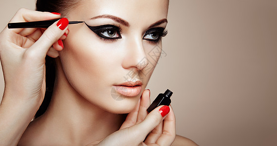 化妆师应用眼影美丽的女人化妆眼与黑色衬里时尚化妆箭红色指甲完美的皮肤图片