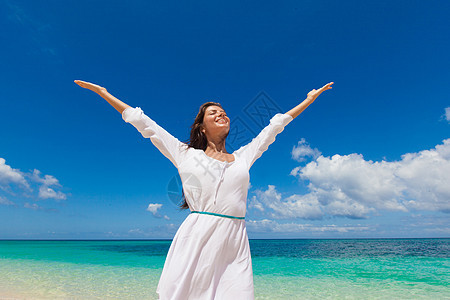 海滩上穿着白色连衣裙的女人穿着白色连衣裙的女人站蓝色的海边背景上,举手图片