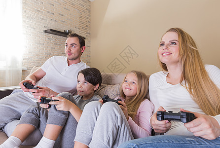 家人玩电子游戏家人两个孩子坐家里的沙发上玩电子游戏图片