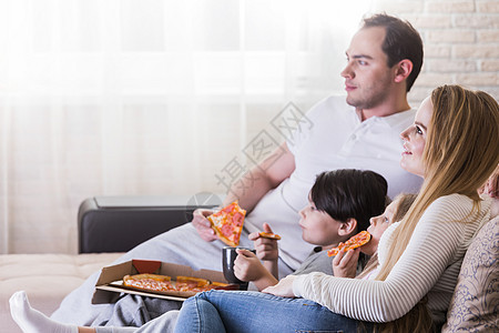 家人看电视轻的父母他们的孩子家里坐沙发上看电视吃披萨微笑图片