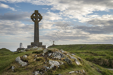 天赛的YnysLlanddwyn岛上的凯尔特十字架与背景景观中的TWRMAWR灯塔图片