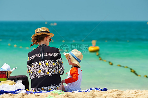 两岁的蹒跚学步的男孩戴着太阳帽,妈妈海滩上图片