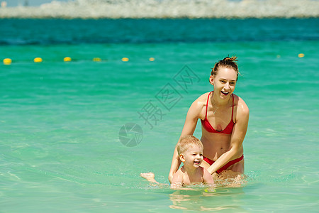 海里游泳快乐的母亲教她的小儿子游泳两岁的蹒跚学步的男孩妈妈海滩上快乐的母亲教她的小儿子游泳背景