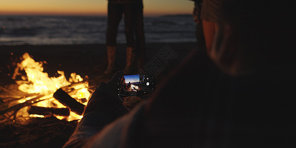 男孩海滩篝火旁给女孩看了张手机上的照片图片