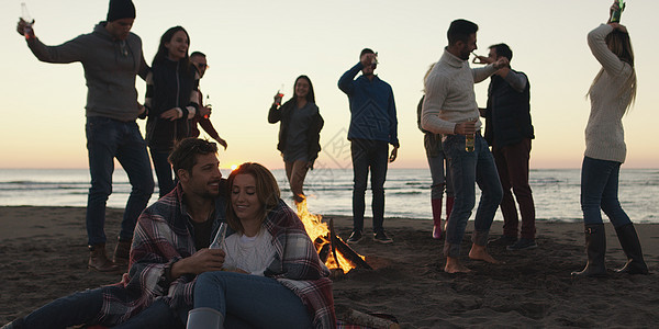 快乐无忧无虑的轻朋友海滩上玩得开心,太阳开始落山的时候篝火旁喝啤酒图片