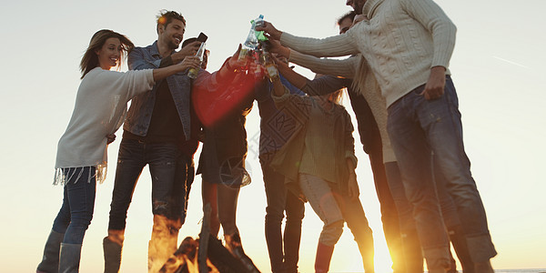 轻的朋友们用啤酒敬酒,秋天的海滩派上围着篝火玩图片
