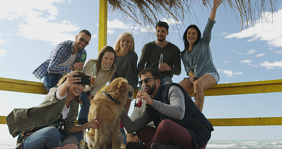 快乐的群朋友海滩屋闲逛,秋天的日子里玩得开心,喝啤酒图片