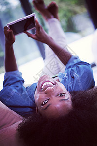 轻的非裔美国妇女家放松她的豪华客厅阅读数字平板电脑上网工作图片