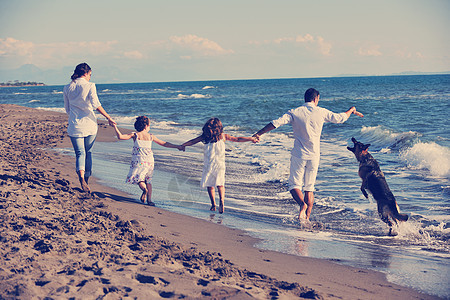 穿着白色衣服的快乐的轻家庭美丽的海滩度假时漂亮的狗玩背景图片