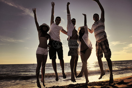 一群年轻朋友们在日落的海滩上跳跃图片
