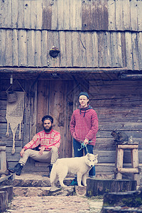 嬉皮士夫妇的肖像,两个轻人白色哈士奇狗坐古老的木制复古房子前旧木屋前装饰图片