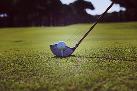 高尔夫球运动员把球放发球台上背景中高尔夫球场景观上美丽的日出高尔夫球运动员把球放发球台上图片