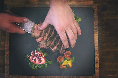 酒店餐厅厨房的厨师手的顶部视图,提供带蔬菜装饰的牛排厨师手端牛排的顶部视图图片