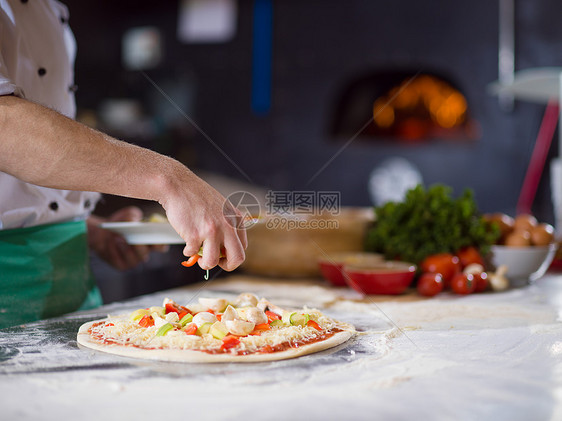 厨师把新鲜蔬菜放厨房桌子上的比萨饼上厨师把新鲜蔬菜放比萨饼上图片