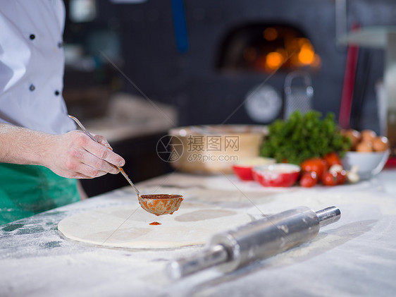 厨师用番茄酱涂抹比萨饼图片