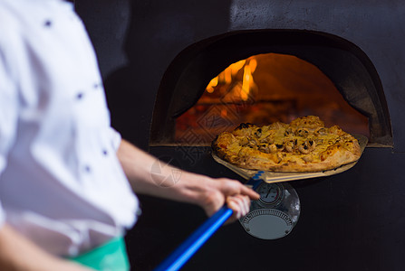 厨师用特殊的铲子把热披萨炉子里出来厨师炉子上热披萨图片