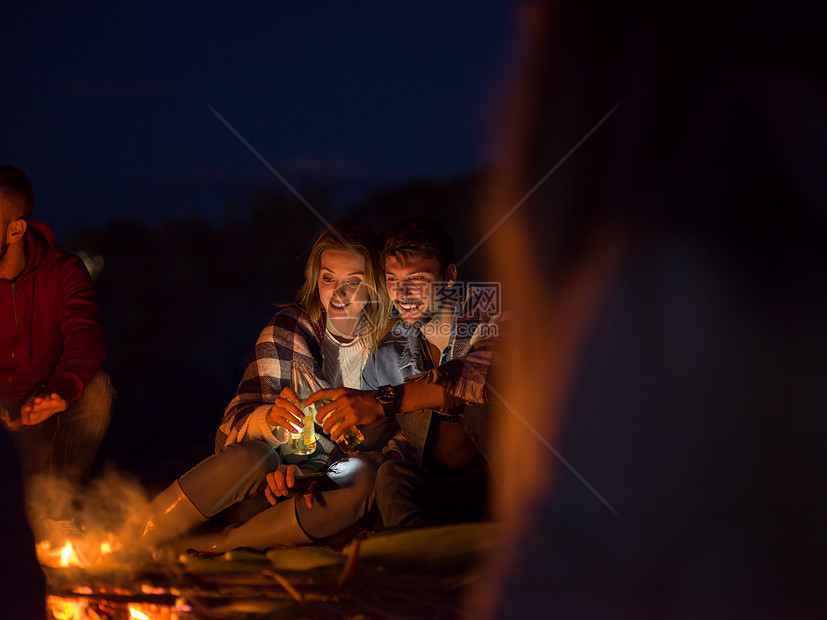 ‘~轻的夫妇晚上朋友坐海滩上的篝火旁喝啤酒夫妇晚上海滩上朋友享受  ~’ 的图片
