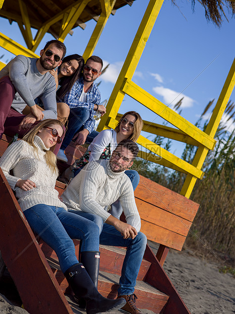 快乐的群朋友海滩屋闲逛秋天的日子里玩得开心喝啤酒群朋友秋天的海滩