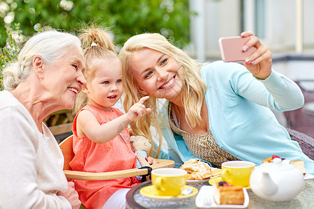 家庭世代人的快乐的母亲女儿祖母咖啡馆餐厅露台用智能手机自拍幸福的家庭咖啡馆自拍图片
