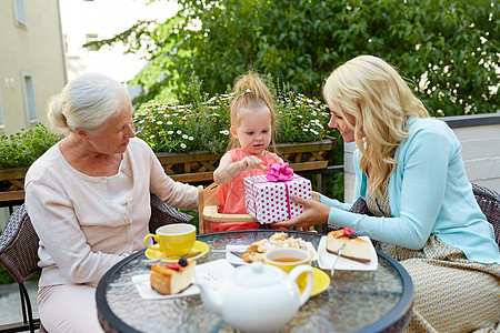 家庭世代人的快乐的祖母母亲咖啡馆餐馆露台给小女儿送礼物快乐的母亲咖啡馆给小女儿送礼物图片