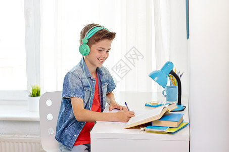 教育,童人的快乐的学生男孩戴着耳机,家里的书笔记本学生男孩戴着耳机写笔记本上图片