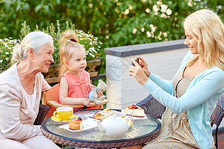 家庭世代人的快乐的微笑母亲与智能手机拍照女儿祖母咖啡馆餐厅露台女人咖啡馆给她的家人拍照图片