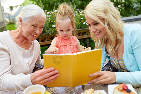 家庭世代人的快乐的微笑母亲与女儿祖母咖啡馆餐厅露台看书快乐的家庭阅读书咖啡馆露台图片