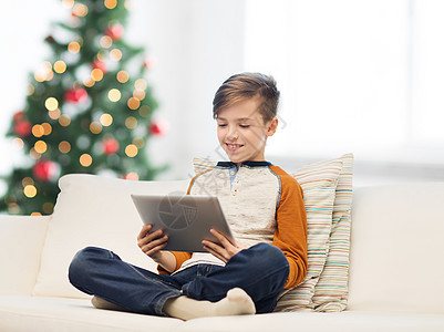 孩子,技术人的微笑的男孩与平板电脑坐沙发上的诞树背景微笑的男孩与平板电脑家里诞节图片