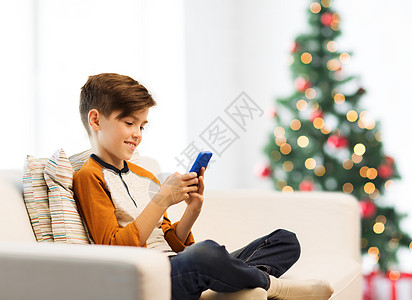 老年人手机孩子,技术,沟通人的微笑男孩与智能手机短信家里玩游戏的诞树背景诞节男孩家里玩智能手机背景