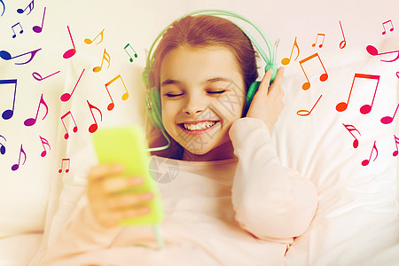 耳机音符人,孩子技术快乐的微笑女孩与智能手机耳机躺床上听音乐的音符戴着耳机床上听音乐的女孩背景