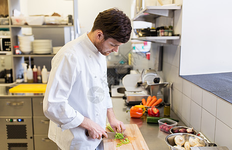 烹饪食物,职业人的快乐的男厨师用刀切芹菜烹饪餐厅厨房的砧板上快乐的男厨师餐厅厨房烹饪食物图片