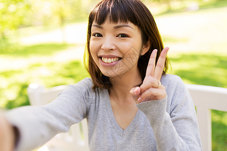 人技术快乐微笑的亚洲妇女公园自拍,并平手标志快乐的亚洲女人自拍并表现出平图片