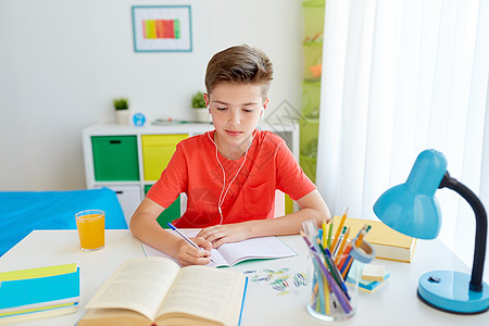 教育,童人的快乐的学生男孩耳机写笔记本书家里学生男孩戴着耳机写笔记本上图片