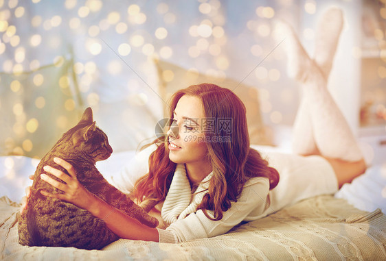 宠物,舒适,休息人的快乐的轻女人猫躺床上家快乐的轻女人,猫躺家里的床上图片