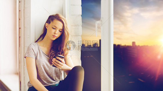 人,技术青少的悲伤,快乐,漂亮的十几岁的女孩坐窗台上,城市背景上用智能手机信息悲伤的漂亮少女,带着智能手图片