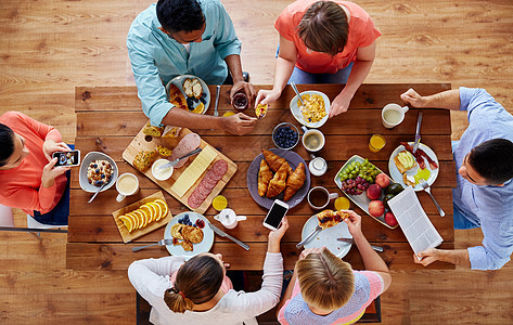 早餐,技术家庭群智能手机的人桌子上吃拍照食物智能手机的人桌子上吃食物图片