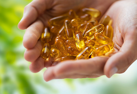 药物,营养补充剂人的密切的手鱼肝油胶囊绿色的自然背景手鱼肝油胶囊图片
