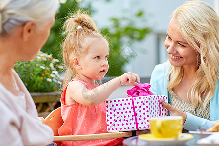 家庭世代人的快乐的祖母母亲咖啡馆餐馆露台给小女儿送礼物快乐的母亲咖啡馆给女儿送礼物图片