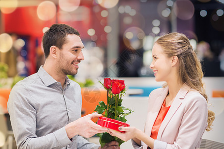 爱情,浪漫,情人节,夫妇人的快乐的轻人带着红花送礼物给微笑的女人购物中心的咖啡馆快乐的情侣商场里礼物鲜花图片